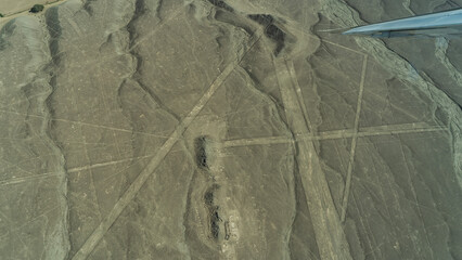 The unique mysterious ancient Nazca lines. Aerial view. Smooth straight and trapezoidal shapes on a sandy plateau. The wing of an airplane in the foreground. Peru.