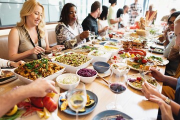 Diverse group enjoying a meal at a table filled with various dishes. People are sharing food, talking, and laughing in a lively dining setting. Festive party dinner with friends.