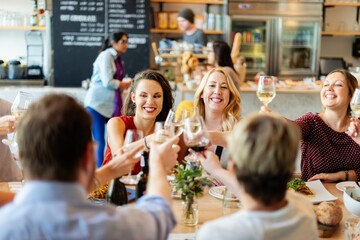 Group of people enjoying a meal, toasting with wine glasses. Lively gathering, diverse group, cheerful atmosphere, celebrating together at a restaurant. Corporate party drinking and networking.