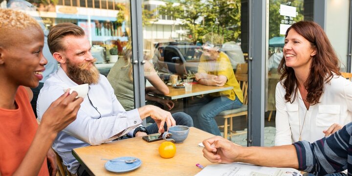 Group of diverse people enjoying coffee at an outdoor cafe. Lively conversation and laughter. Friends gathering, sharing stories, and sipping coffee together. Diverse friends in cafe.