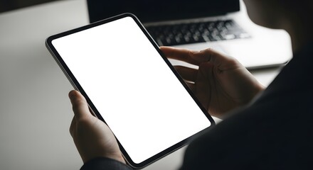 Woman holds a tablet with a blank white screen using it for work or entertainment with a laptop in t