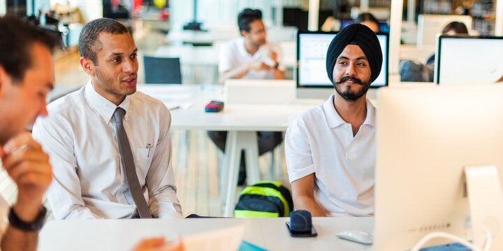 Diverse office meeting with professionals collaborating. Men in business attire, focused on teamwork and discussion. Bright, modern workspace setting. Young professionals in open workspace at company.