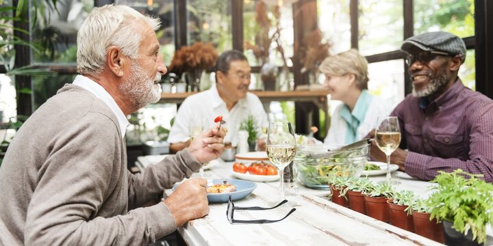 Group of diverse seniors enjoying a meal together. Elderly friends, diverse backgrounds, sharing food, laughter, and conversation in a cozy setting. Retired friends having a lunch party. - Powered by Adobe