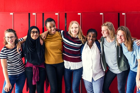 Diverse group of girls, including different ethnicities, standing together at lockers and smiling. Girls front of red lockers, women showing unity and friendship. Diverse teenage students at school. - Powered by Adobe