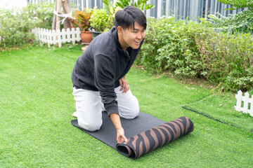 Man rolling yoga mat on green grass outdoors smiling and enjoying exercise in garden