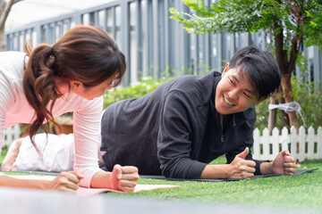 Two people exercising outdoors on grass, smiling and engaging in plank workout together, enjoying healthy and active lifestyle in garden setting