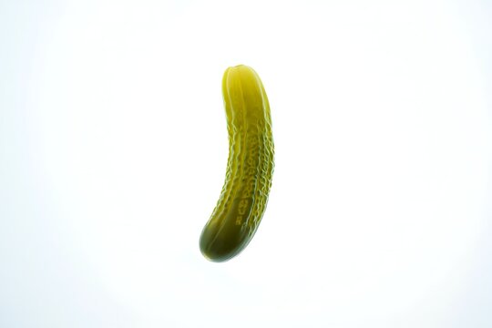 A single dill pickle, slightly curved, stands vertically against a bright white background.