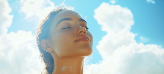 A serene young woman with her eyes closed peacefully enjoys the tranquil outdoor setting basking in the natural light and calming blue sky  This image evokes a sense of relaxation contemplation