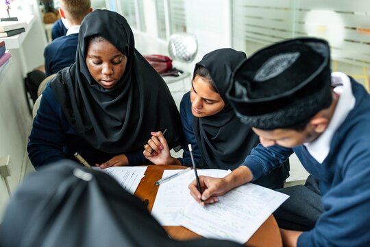 Diverse group of Muslim students studying together, focused on notes. Diverse Muslim students wearing traditional school attire, collaborating on assignments. School work education. - Powered by Adobe