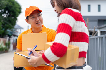 Delivery worker in orange uniform handing parcel to woman signing clipboard outdoors, residential area background, friendly interaction and service