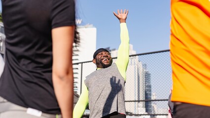Group outdoor exercise session with diverse participants. Energetic man in gray and neon sportswear leads the workout, smiling and raising his hand enthusiastically. Teamwork happy outdoor activity,