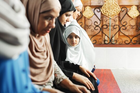 A group of Muslim women, including a young girl, sit together in a serene setting. The Muslim women, dressed in hijabs, reflect a sense of community and spirituality.