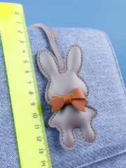 Close-up of a fashionable gray  leather rabbit keychain with a bow, attached to a blue stylish bag