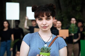 Young woman holding a plant at a protest. The woman in protest with diverse group of people with protest signs. Young diverse people in environment protest, young woman protest for environment