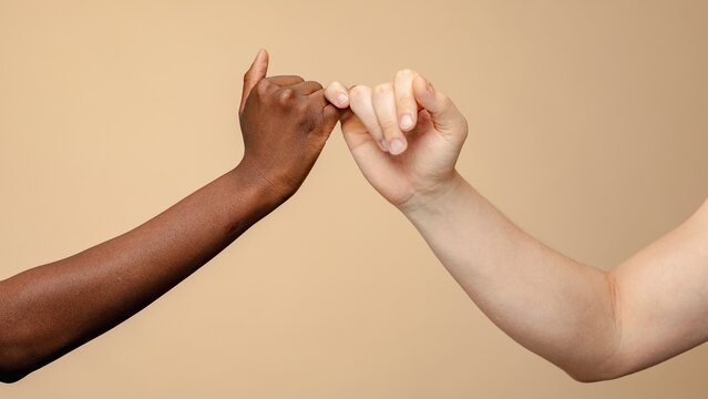 Two hands making a pinky promise against a neutral background. The gesture symbolizes trust and friendship. Pinky promise signifies a bond and commitment. Diverse people connecting, focus on arms.