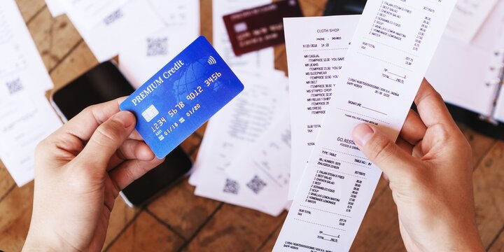 Hands holding a credit card and receipts. Credit card and receipts suggest shopping or budgeting. Credit card use and receipt management are key themes. Finance and budgeting, paying with credit card.