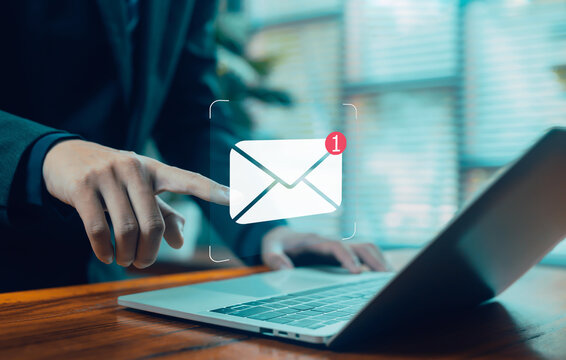 A business professional touching a floating email notification icon above a laptop, representing digital communication, online messaging, business alerts, connectivity, modern workplace interaction.