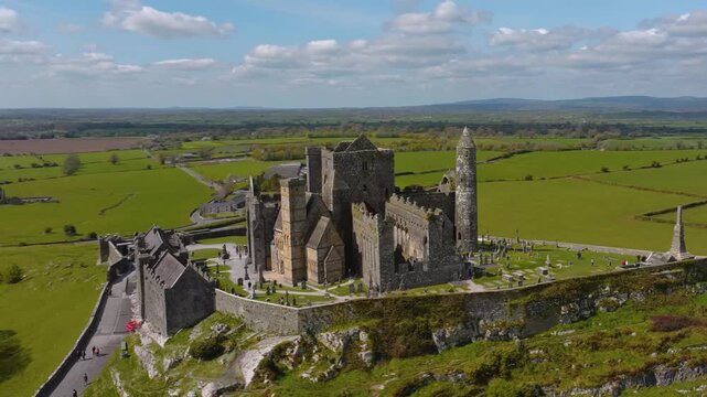 4K Aerial view of the Rock of Cashel, capturing ancient stone walls, round towers, and cathedral ruins surrounded by rolling green fields and historic farmland. Co.Tipperary, Ireland_018
