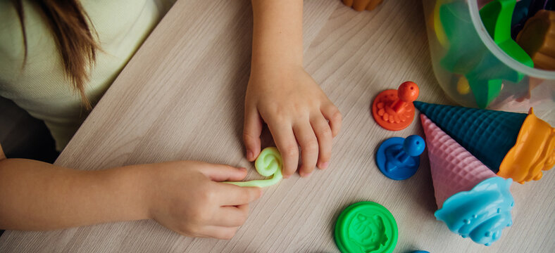 A little girl makes figurines out of colored airy plasticine, modeling dough. Hobbies for children's creativity, educational activities, development of fine motor skills of hands.