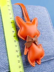 Close-up of a fashionable orange leather fox keychain with a bow, attached to a blue stylish bag
