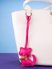 Close-up of a fashionable pink   leather cat-shaped keychain with a bow, attached to a white stylish bag