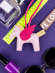 Close-up of a fashionable leather pegasus keychain with vibrant pink wings on purple table with women accessories