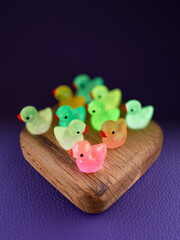 Close-up of a group of small, glowing, fun figurines of multicolored ducks on a wooden podium