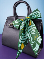 Close-up of a silk ribbon bow with a tropical leaf pattern on a black leather bag