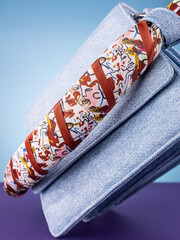 Close-up of a dark red silk ribbon  with an art face pattern on a blue leather bag