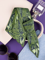 Close-up of a silk ribbon with a tropical leaf pattern   on purple table with women accessories