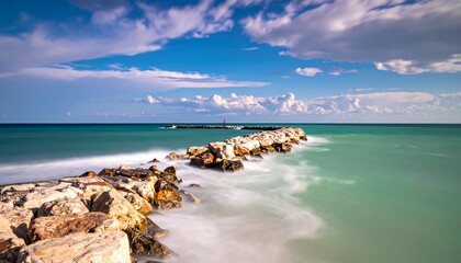 Long exposure of a rocky breakwater stretching into the ocean under a cloudy sky.
