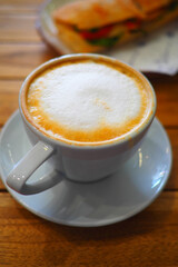 Coffee sits on a table beside a sandwich at a cafe