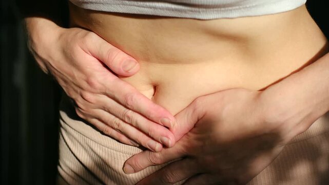 Young woman suffering from abdominal pain, holding her stomach with both hands and massaging her belly to relieve cramps from painful menstruation, indigestion, or gastritis problems
