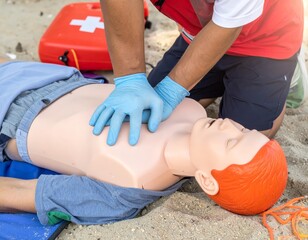 Lifeguard placing electrodes on cpr training dummy on beach. Safety concept