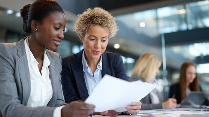 Two diverse businesswomen collaborating on documents in a modern office, discussing project plans with focus and teamwork. - Powered by Adobe