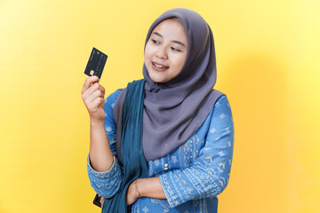 Woman in hijab holding credit card against yellow background.