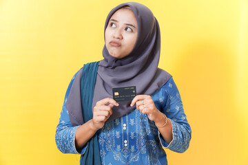 Woman in hijab holds credit card, looking thoughtful.
