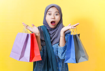 Surprised woman in hijab with shopping bags on yellow background.