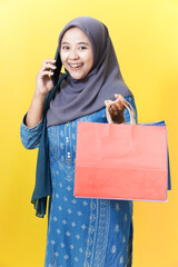 Smiling woman in hijab with shopping bag talking on phone.