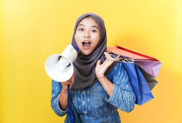 Excited Muslim woman with megaphone and shopping bags on yellow background.