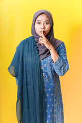 Woman in hijab gesturing silence on yellow background.