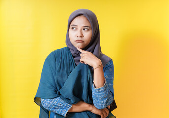 Thoughtful woman in hijab against yellow backdrop.