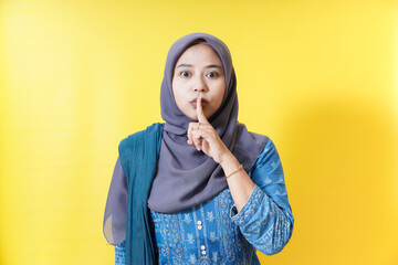 Woman in hijab gesturing silence on yellow background.