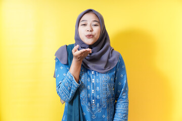 Woman in hijab blowing kiss on yellow background.