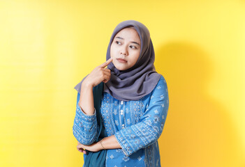 Woman in hijab thinking on yellow background.
