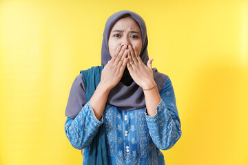 Shocked Muslim woman covering mouth on yellow background.