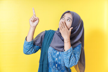 Woman in hijab pointing up, surprised.