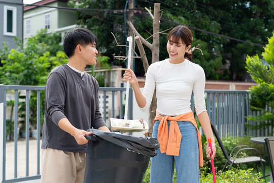 Young couple cleaning garden together with broom and dustpan, enjoying outdoor activity