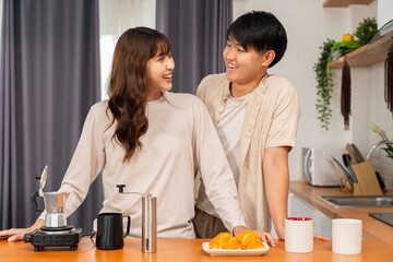 Young couple smiling and enjoying morning coffee with croissants in kitchen