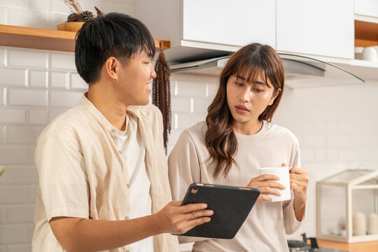 Young couple using digital tablet and drinking coffee in kitchen, casual lifestyle moment